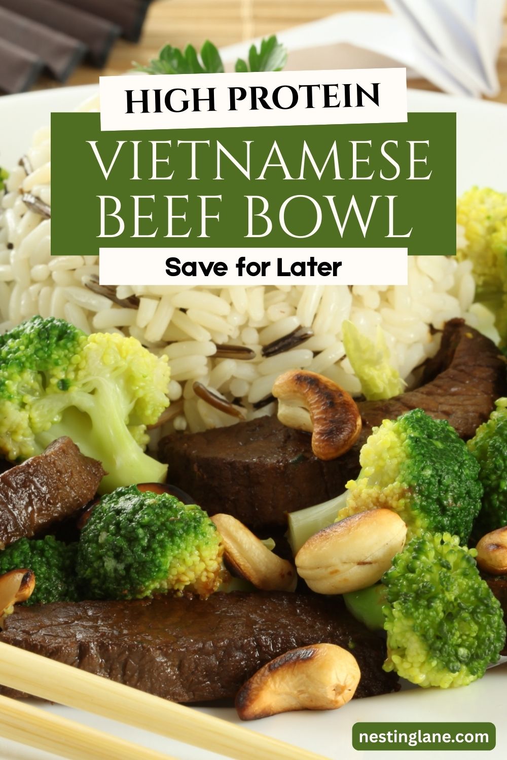 A close-up of a high protein Vietnamese beef bowl with sliced beef, broccoli florets, toasted cashews, and mixed white and wild rice on a plate. Chopsticks rest on the edge of the dish. Text overlay reads “High Protein Vietnamese Beef Bowl” and “Save for Later,” with nestinglane.com in the corner.