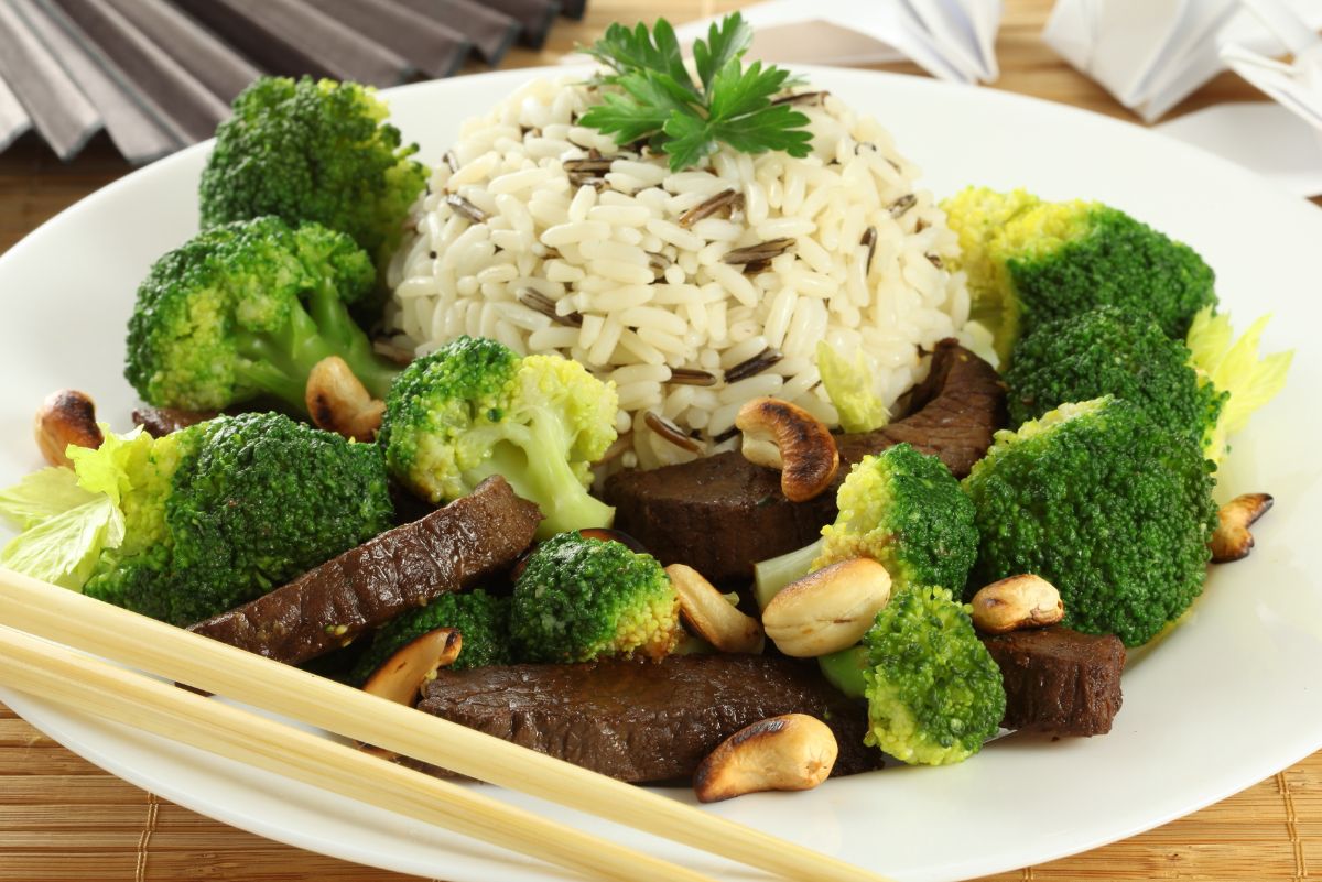 High protein Vietnamese beef bowl with sliced beef, steamed broccoli florets, toasted cashews, and a mound of white and wild rice on a white plate. Wooden chopsticks rest on the plate, with a parsley garnish on the rice.