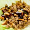 Hoisin ground beef lettuce wrap filled with seasoned ground beef, diced onions, and toasted peanuts, drizzled with glossy hoisin sauce. The savory beef mixture sits in a crisp pale green lettuce leaf, shown close up to highlight the texture and toppings.