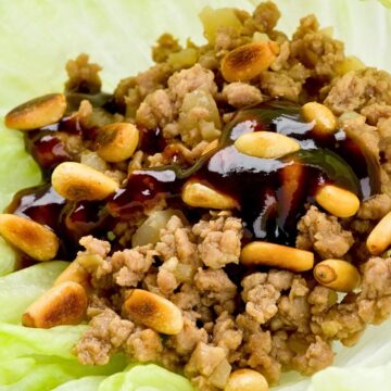 Hoisin ground beef lettuce wrap filled with seasoned ground beef, diced onions, and toasted peanuts, drizzled with glossy hoisin sauce. The savory beef mixture sits in a crisp pale green lettuce leaf, shown close up to highlight the texture and toppings.
