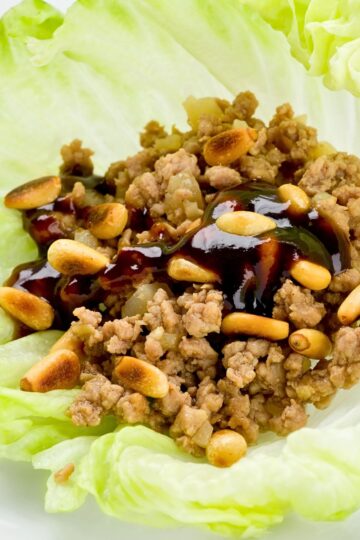 Hoisin ground beef lettuce wrap filled with seasoned ground beef, diced onions, and toasted peanuts, drizzled with glossy hoisin sauce. The savory beef mixture sits in a crisp pale green lettuce leaf, shown close up to highlight the texture and toppings.