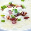 Creamy loaded potato soup in a white bowl topped with chopped turkey bacon, sliced green onions, and a dollop of sour cream. Thick, smooth potato soup texture with crispy bacon pieces and fresh scallions visible on top, styled as a healthier comfort food soup.