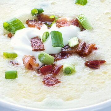 Creamy loaded potato soup in a white bowl topped with chopped turkey bacon, sliced green onions, and a dollop of sour cream. Thick, smooth potato soup texture with crispy bacon pieces and fresh scallions visible on top, styled as a healthier comfort food soup.