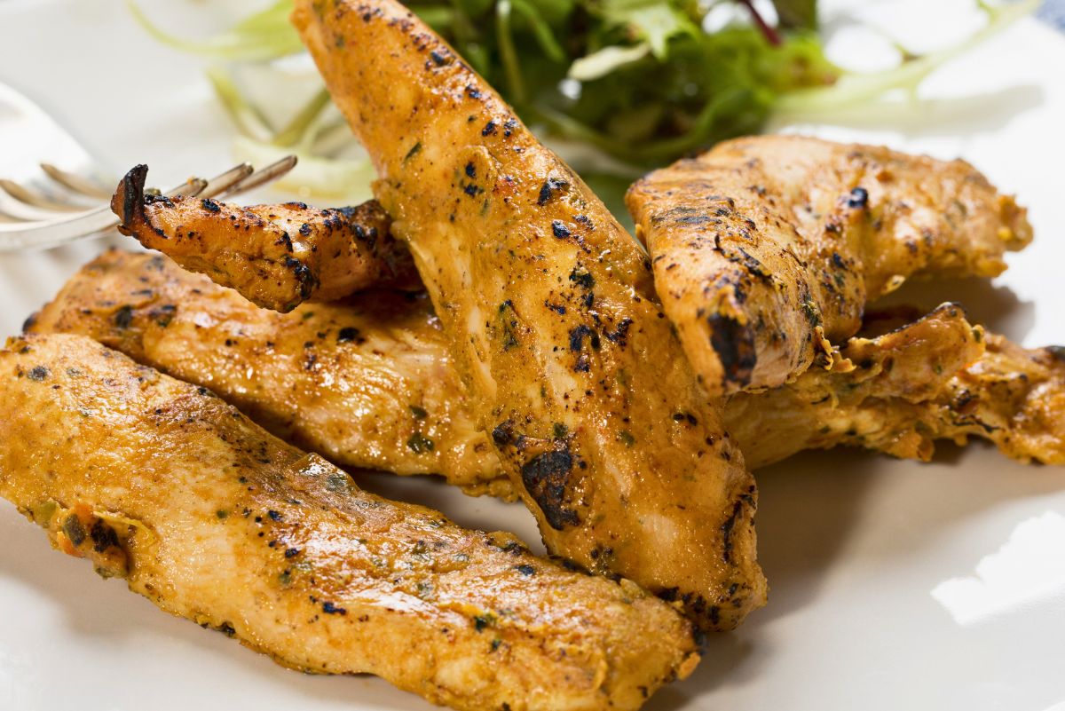 Smoky chipotle peanut chicken tenders with a golden, lightly charred crust arranged on a white plate. Juicy grilled chicken strips show visible seasoning and grill marks, with mixed leafy greens in the background for a simple, savory chicken dinner presentation.