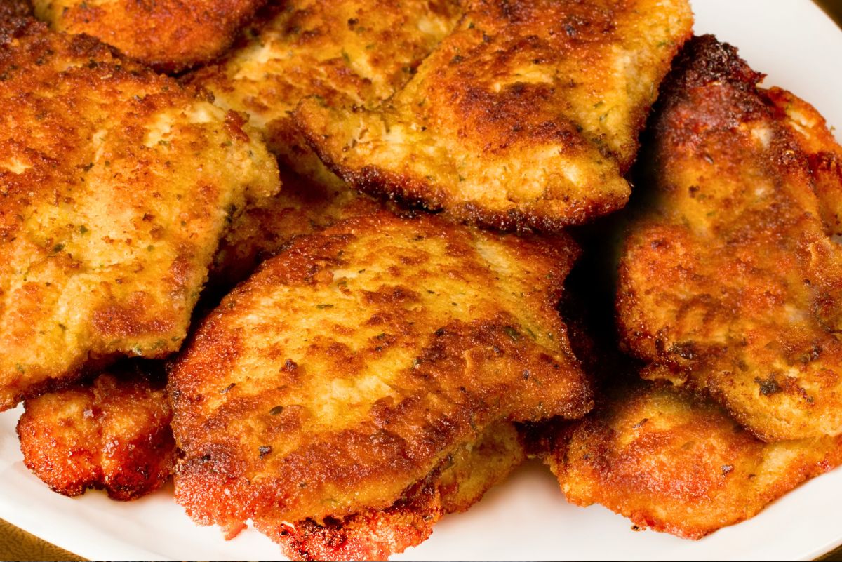 Close-up of crispy skillet Parmesan chicken piled on a white plate. Breaded chicken pieces are golden brown with darker crunchy edges and a homemade pan-fried look, shown in a tight food photo with no text.
