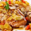Close-up of baked almond apricot chicken breasts with glossy apricot sauce, sliced toasted almonds, diced apricots, and red pepper on a white plate. Fresh thyme garnish on top, with a soft blurred background.