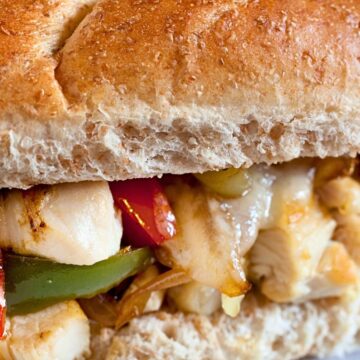 Close-up of a chicken Philly sub on a whole wheat roll with grilled chicken, melted cheese, red and green bell peppers, and sautéed onions. High protein sandwich with a soft hoagie bun and savory filling.