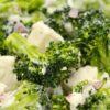 Close-up of creamy broccoli feta salad in a white bowl with fresh broccoli florets, crumbled feta, diced red onion, and creamy dressing. Healthy broccoli salad with bright green vegetables and chunky cheese pieces.