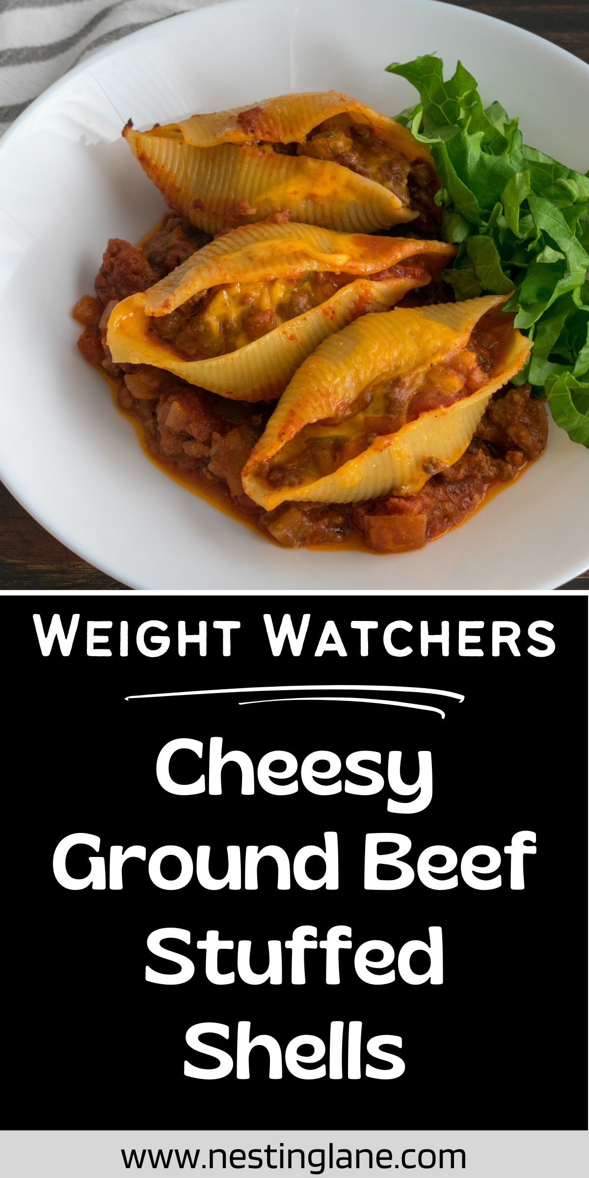 White bowl of cheesy ground beef stuffed shells in tomato sauce, topped with a side of leafy greens. Large pasta shells are filled with beef and melted cheese. Black text panel reads “WEIGHT WATCHERS Cheesy Ground Beef Stuffed Shells.” Bottom text says “www.nestinglane.com”