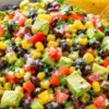 Avocado corn black bean salad with tortilla chips, diced avocado, corn, tomatoes, black beans, red onion, bell pepper, and cilantro in a speckled bowl.