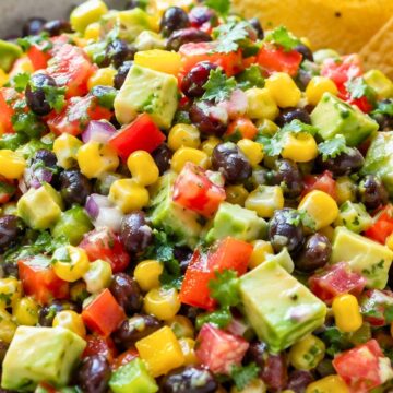 Avocado corn black bean salad with tortilla chips, diced avocado, corn, tomatoes, black beans, red onion, bell pepper, and cilantro in a speckled bowl.