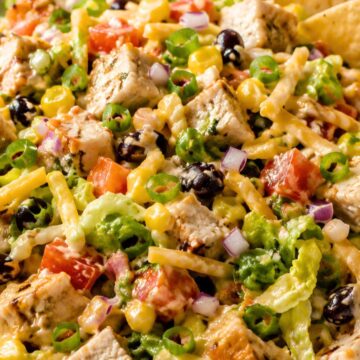 BBQ chicken chopped salad with grilled chicken, lettuce, black beans, corn, tomatoes, red onion, shredded cheese, green onions, and tortilla chips in a bowl.