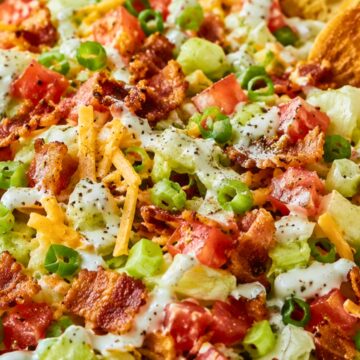 BLT chopped salad with iceberg lettuce, diced tomatoes, crispy bacon, green onions, shredded cheddar cheese, creamy ranch dressing, and toasted sourdough chips in a white bowl.