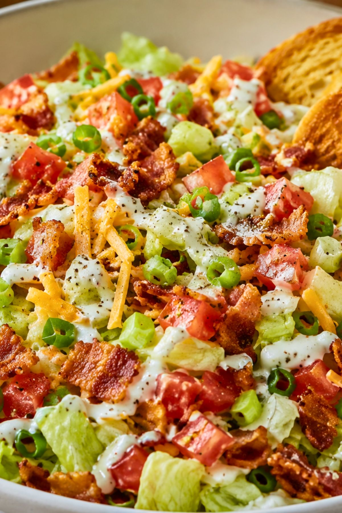 BLT chopped salad with iceberg lettuce, diced tomatoes, crispy bacon, green onions, shredded cheddar cheese, creamy ranch dressing, and toasted sourdough chips in a white bowl.