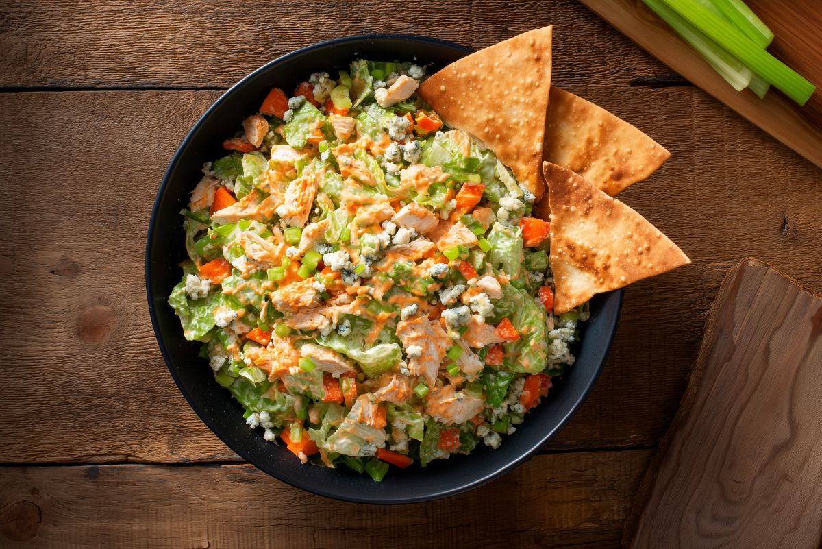 Buffalo chicken chopped salad with diced chicken, lettuce, celery, bell peppers, blue cheese, Buffalo dressing, and crispy chips in a black bowl.