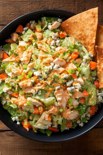 Buffalo chicken chopped salad with lettuce, celery, red bell peppers, blue cheese crumbles, creamy Buffalo dressing, and crispy chips.