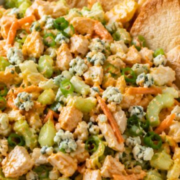 Buffalo chicken chopped salad close-up with diced chicken, lettuce, celery, carrots, green onions, blue cheese crumbles, buffalo ranch dressing, and toasted pita chips in a white bowl.