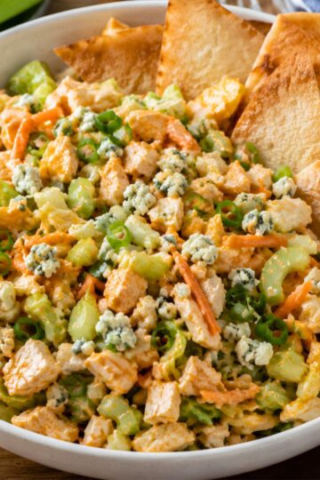 Buffalo chicken chopped salad close-up with diced chicken, lettuce, celery, carrots, green onions, blue cheese crumbles, buffalo ranch dressing, and toasted pita chips in a white bowl.