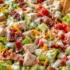 Chicken bacon ranch chopped salad with diced chicken, crisp bacon, lettuce, cucumbers, tomatoes, shredded cheddar cheese, creamy ranch dressing, and pita chips served in a bowl.