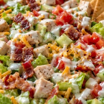 Chicken bacon ranch chopped salad with diced chicken, crisp bacon, lettuce, cucumbers, tomatoes, shredded cheddar cheese, creamy ranch dressing, and pita chips served in a bowl.