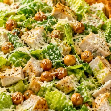 High protein chicken Caesar chopped salad with romaine lettuce, grilled chicken, roasted chickpeas, Parmesan cheese, creamy Caesar dressing, and garlic pita chips in a bowl.