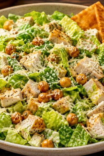 High protein chicken Caesar chopped salad with romaine lettuce, grilled chicken, roasted chickpeas, Parmesan cheese, creamy Caesar dressing, and garlic pita chips in a bowl.