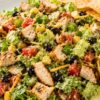 Chicken fajita chopped salad with grilled chicken, romaine lettuce, black beans, corn, tomatoes, cheddar cheese, creamy dressing, and tortilla chips on a white plate.