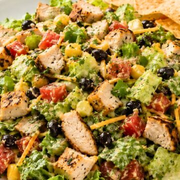 Chicken fajita chopped salad with grilled chicken, romaine lettuce, black beans, corn, tomatoes, cheddar cheese, creamy dressing, and tortilla chips on a white plate.