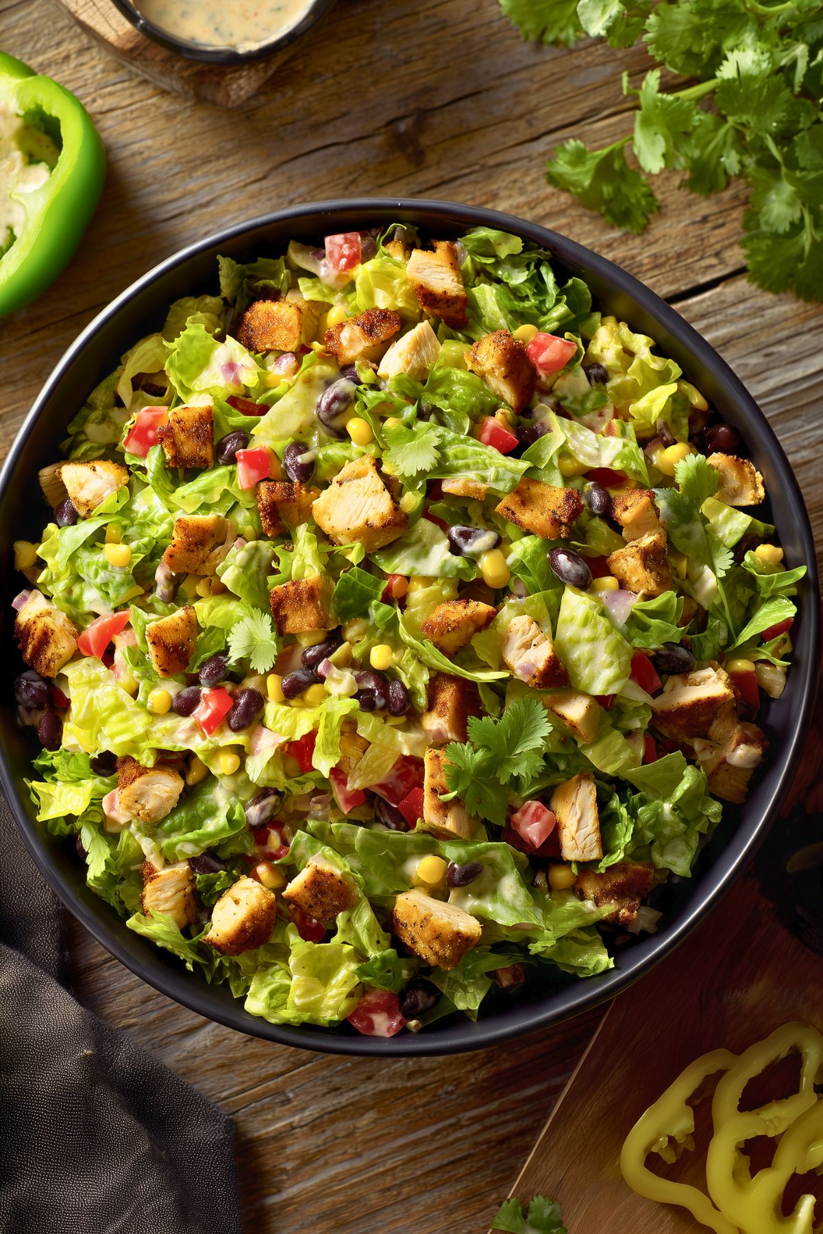 Chicken fajita chopped salad in a black bowl with grilled chicken, romaine lettuce, black beans, corn, tomatoes, cilantro, and creamy dressing on a rustic wood table.