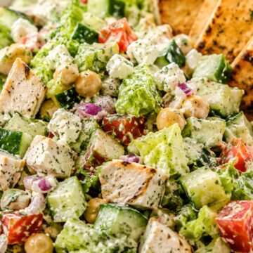 Chicken gyro chopped salad with grilled chicken, romaine, cucumber, tomatoes, chickpeas, red onion, feta, creamy tzatziki-style dressing, and toasted pita chips in a shallow bowl.