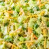 Dill pickle chopped salad with creamy ranch dressing, chopped lettuce, cucumber, dill pickles, shredded carrots, cheddar cheese, and green onions in a speckled bowl.