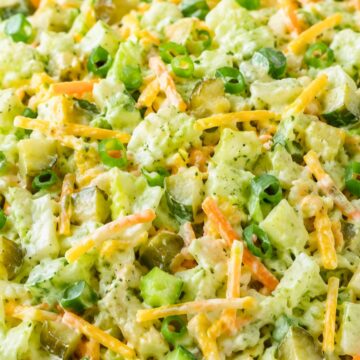 Dill pickle chopped salad with creamy ranch dressing, chopped lettuce, cucumber, dill pickles, shredded carrots, cheddar cheese, and green onions in a speckled bowl.