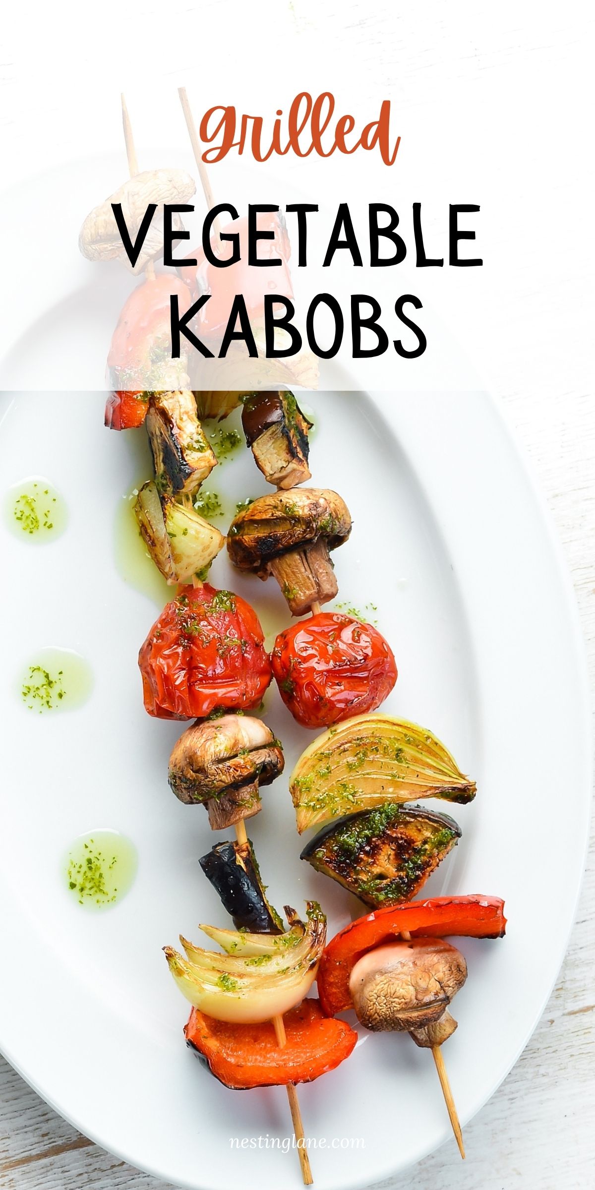 Grilled vegetable kabobs with mushrooms, tomatoes, onion, red bell pepper, eggplant, and green herb oil on a white plate. Text reads “Grilled Vegetable Kabobs” and “nestinglane.com.”