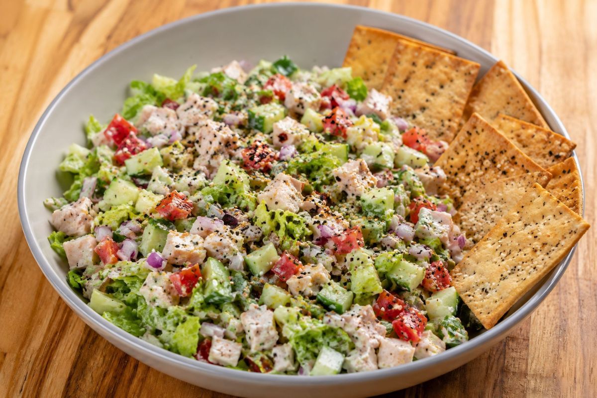 Everything bagel chopped salad with diced chicken, romaine lettuce, cucumbers, tomatoes, red onion, creamy dressing, and everything bagel seasoning in a shallow bowl with bagel chips for scooping.