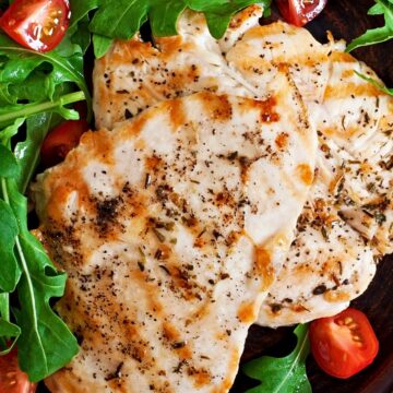 Garlic herb chicken breast served with fresh arugula and cherry tomatoes on a dark plate for a healthy high protein dinner or salad recipe.