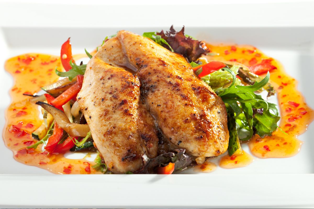 Grilled chicken breasts with sweet chili glaze served over fresh greens, red bell pepper, mushrooms, and sauce on a white rectangular plate.