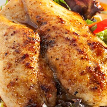 Grilled chicken breasts with sweet chili glaze served over fresh greens, red bell pepper, and leafy salad on a white plate.