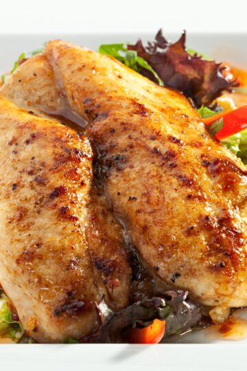 Grilled chicken breasts with sweet chili glaze served over fresh greens, red bell pepper, and leafy salad on a white plate.