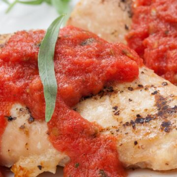 Grilled chicken breast topped with chunky fresh tomato tarragon sauce and a green tarragon leaf on a white plate.