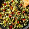 Italian chopped salad with finely chopped lettuce, chickpeas, red bell peppers, black olives, banana peppers, red onion, and garlic pita chips in a black bowl.