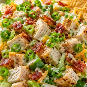 JalapeƱo popper chicken chopped salad with grilled chicken, bacon, shredded cheddar, jalapeƱos, green onions, lettuce, creamy dressing, and tortilla chips in a speckled bowl.
