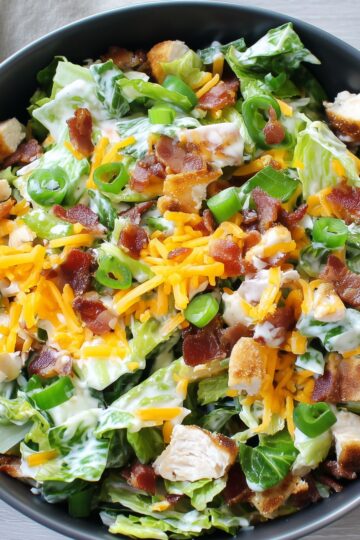 Close-up of jalapeño popper chicken salad with chopped romaine, chicken, bacon, cheddar cheese, green onions, jalapeños, and creamy dressing.