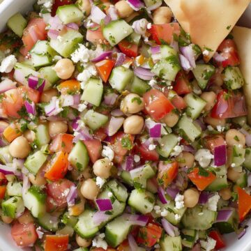 Mediterranean cucumber tomato chopped salad with chickpeas, red onion, feta cheese, fresh herbs, and a toasted pita chip.