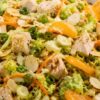 Close-up sesame chicken chopped salad with diced chicken, mandarin oranges, romaine, cabbage, carrots, sliced almonds, green onions, and sesame ginger dressing in a shallow bowl.