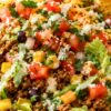 Close-up of a high-protein street taco chopped salad in a bowl. Features chopped romaine lettuce, seasoned ground beef, black beans, corn, diced tomatoes, shredded cheese, cilantro, and a creamy dressing drizzle. Tortilla chips are visible on the side, emphasizing a fresh and colorful Tex-Mex style salad.