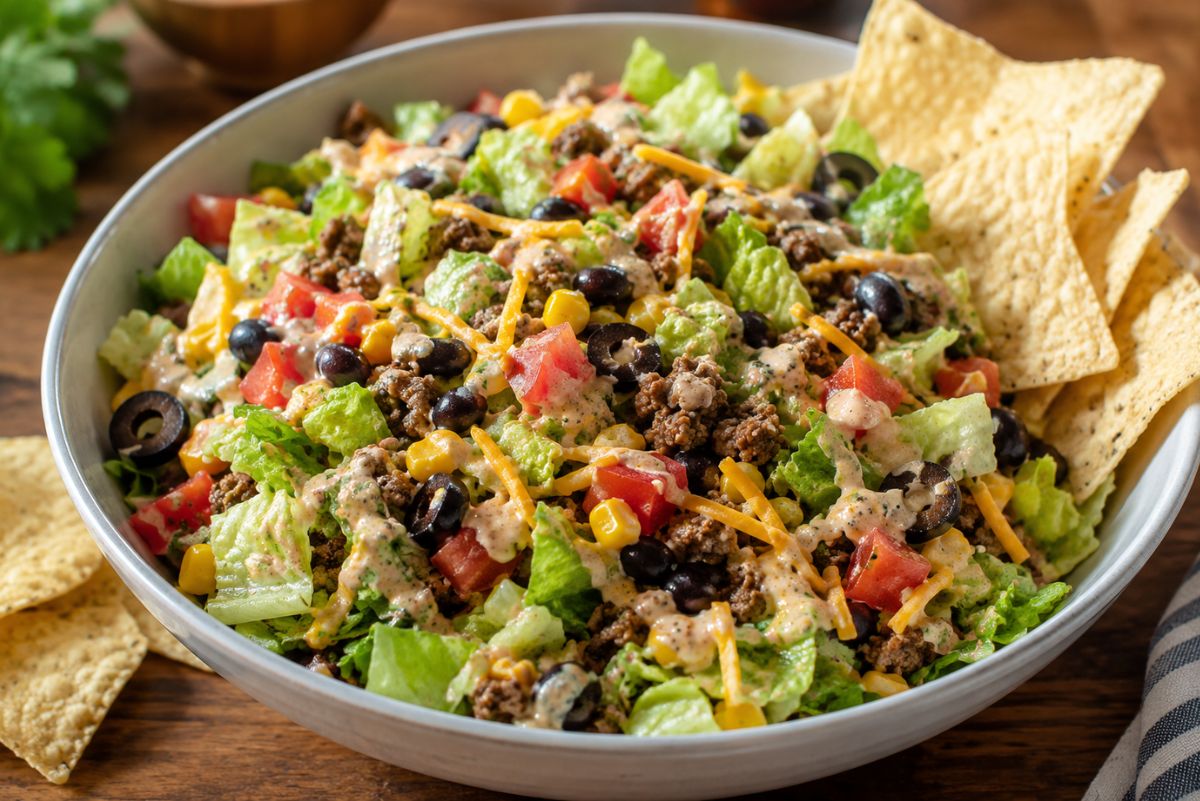 Taco chopped salad with romaine lettuce, seasoned ground beef, black beans, corn, tomatoes, shredded cheddar, black olives, creamy taco ranch dressing, and tortilla chips for scooping.