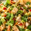 Thai peanut chicken chopped salad with chopped chicken, romaine, cabbage, carrots, red bell pepper, green onions, cilantro, creamy peanut dressing, and crispy wonton chips in a shallow bowl.