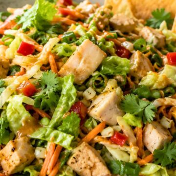 Thai peanut chicken chopped salad with chopped chicken, romaine, cabbage, carrots, red bell pepper, green onions, cilantro, creamy peanut dressing, and crispy wonton chips in a shallow bowl.