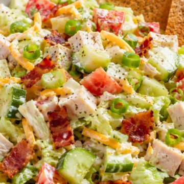 Turkey club chopped salad with toast chips, diced turkey, bacon, lettuce, tomato, cucumber, cheddar cheese, green onions, and creamy dressing in a large bowl.