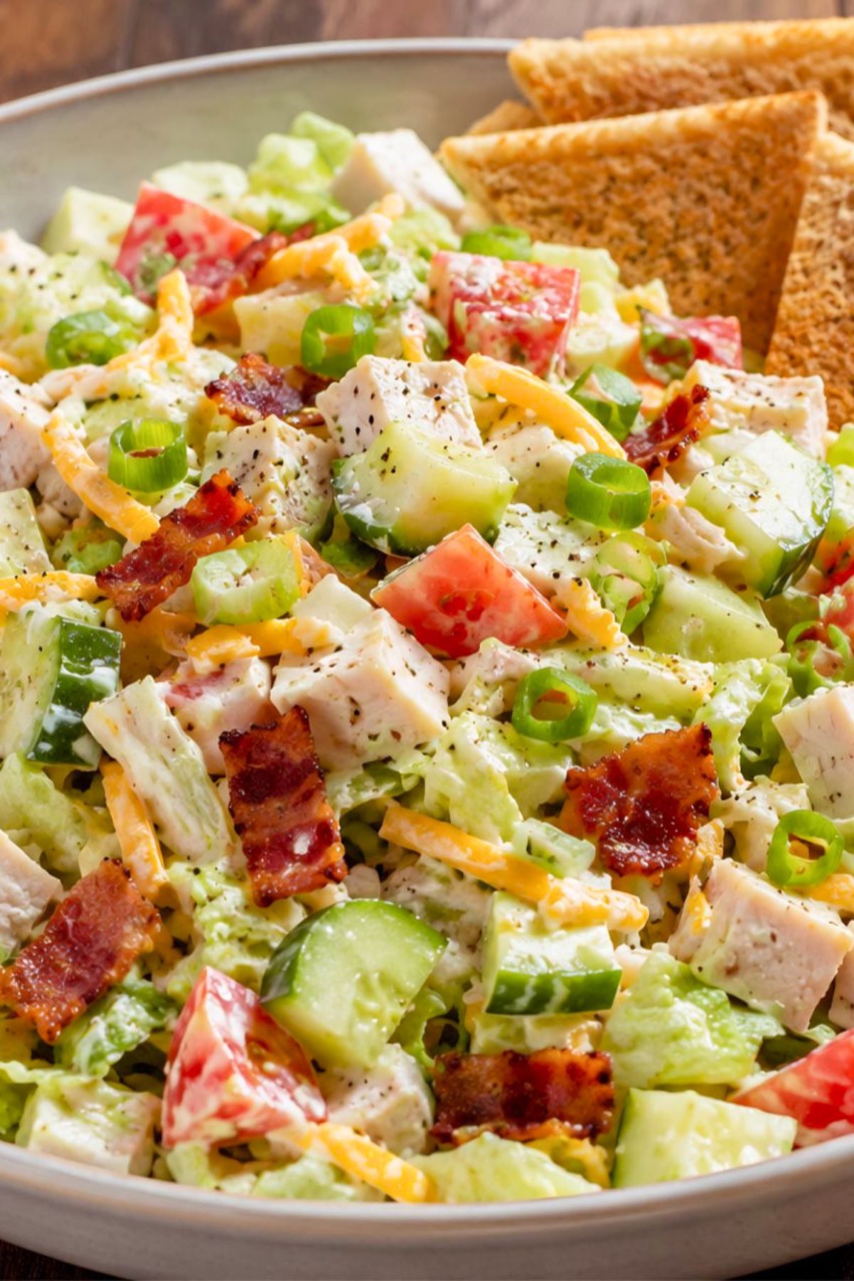 Turkey club chopped salad with toast chips, diced turkey, bacon, lettuce, tomato, cucumber, cheddar cheese, green onions, and creamy dressing in a large bowl.
